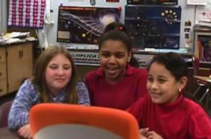 Three young students look at a computer monitor